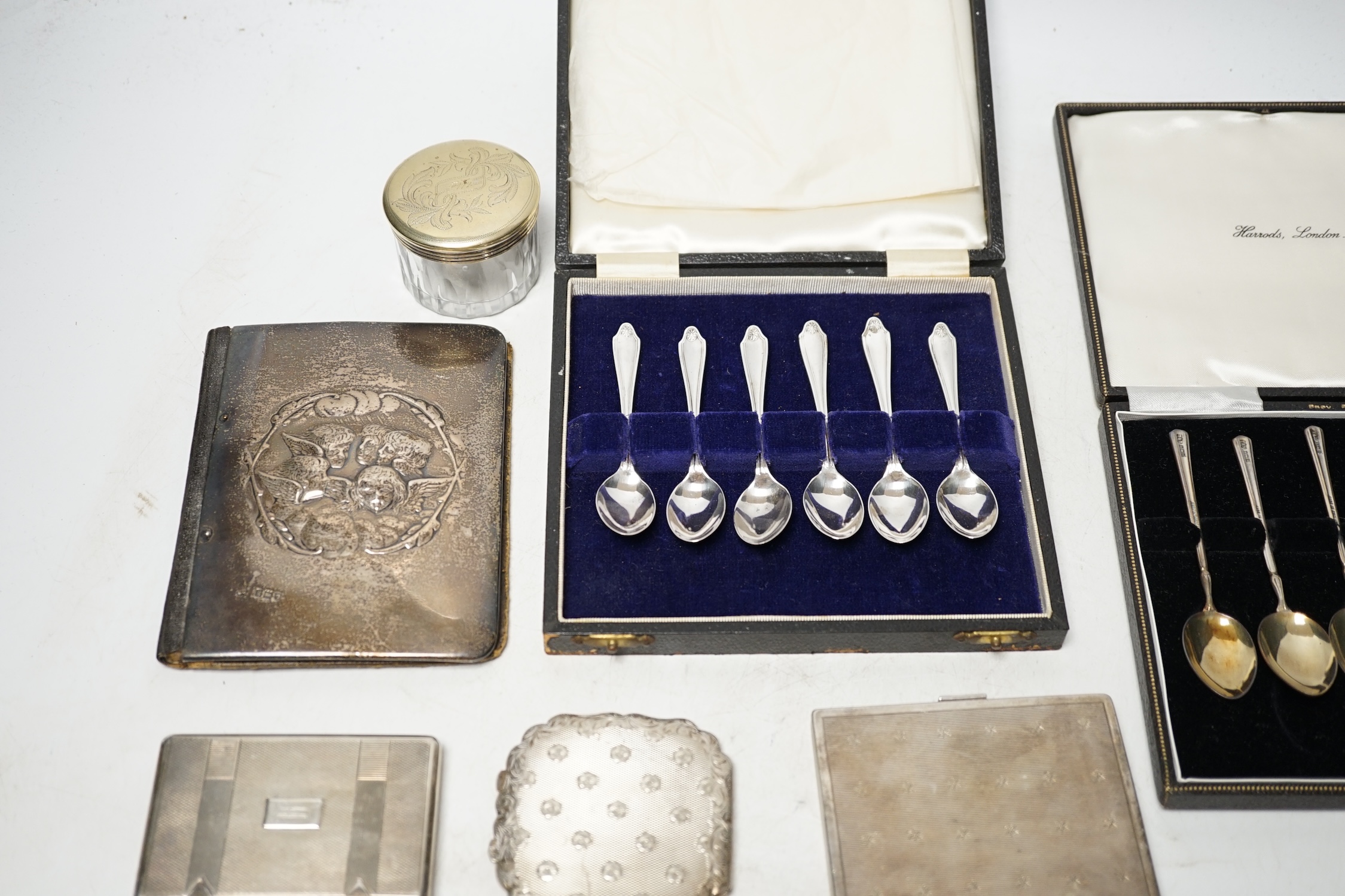 Two cased sets of six silver coffee spoons, a silver mounted leather case, two white metal cigarette cases, a white metal compact and a toilet jar. Condition - poor to fair